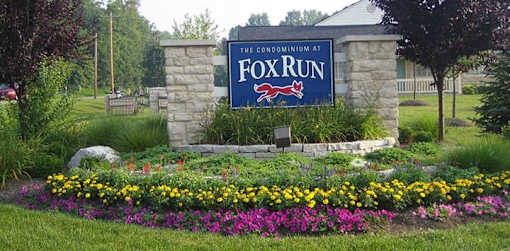 A sign that says "The Condominium at Fox Run" is surrounded by flowers.