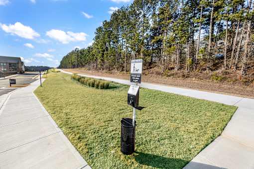 A signpost with a walking person symbol stands on a grassy area next to a paved walkway.