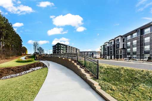 A long concrete walkway leads to a building with a black fence on one side.