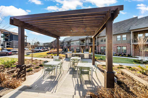 A wooden pergola with green chairs and tables is in the foreground of a residential area.