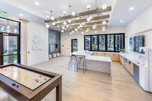 A room with a pool table in the foreground and a kitchen area in the background.