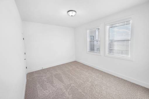 A room with a carpeted floor and two windows with blinds.