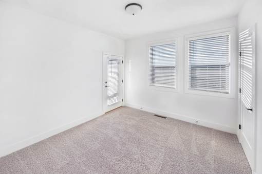 A room with a carpeted floor and two windows with blinds.