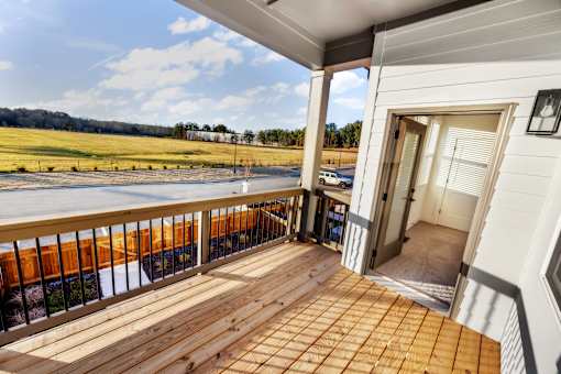 A wooden deck with a white house and a field in the background.