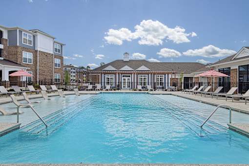 A large swimming pool with lounge chairs and umbrellas in front of a building.