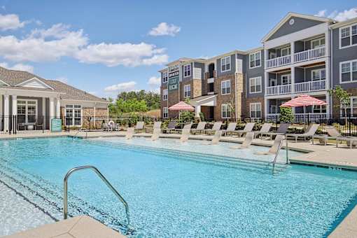A swimming pool with lounge chairs and umbrellas in front of a multi-story apartment building.