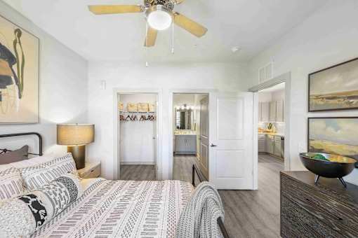 A bedroom with a bed, a ceiling fan, and a painting on the wall.