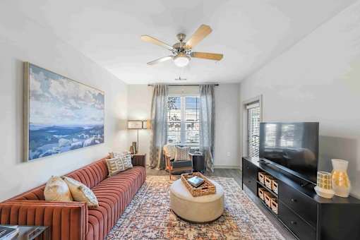 A living room with a red couch, a ceiling fan, and a large painting on the wall.