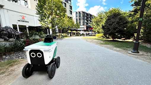 A small white and black robotic vehicle is driving down a city street. at West Inman Lofts, Atlanta