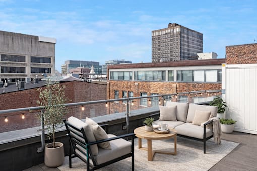 A balcony with a chair, couch, and table with a view of the city.