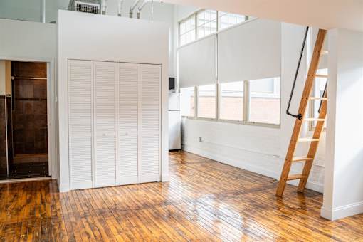 A room with a wooden floor and a white wall with a ladder leaning against it.