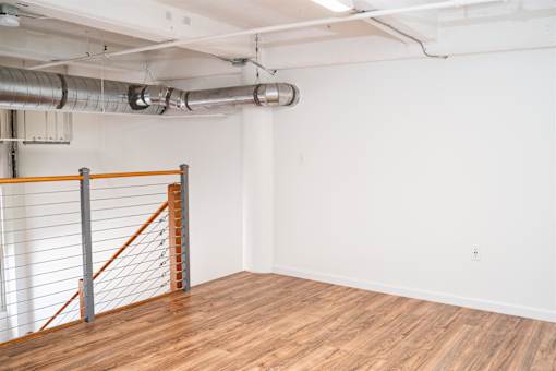 A room with a wooden floor and a white wall with a metal railing on the left side.