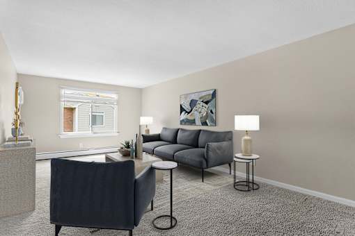 A living room with a grey sofa, a black chair, and a small table with a lamp on it at Rose Hill Estates, Norwich, CT, 06360