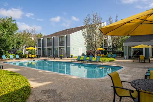 A pool area with chairs and umbrellas in front of a building.