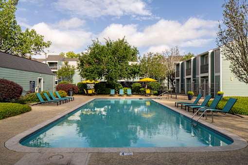 A small pool surrounded by lawn chairs and trees.