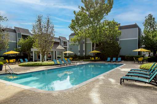 A swimming pool surrounded by lounge chairs and umbrellas in front of a building.
