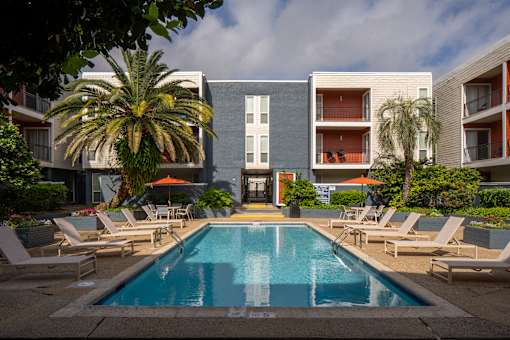 A swimming pool surrounded by lounge chairs and palm trees in front of a modern apartment building.
