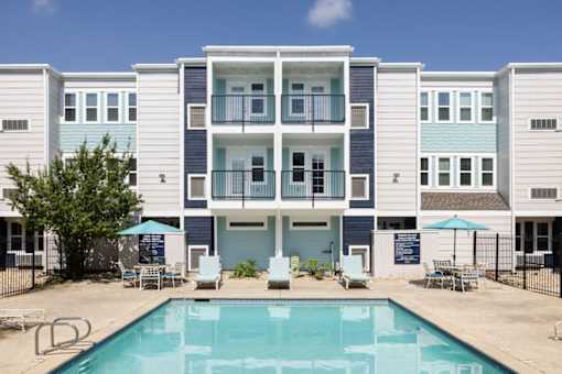 A swimming pool is in front of a row of apartment buildings.