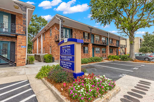 A sign for the Tonni Gardens Apartments is in front of a brick building.