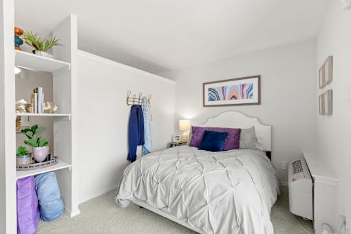 A white bedroom with a white bed and a white shelf with plants on it.