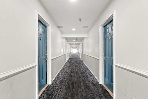 A long hallway with blue doors and carpeted flooring.