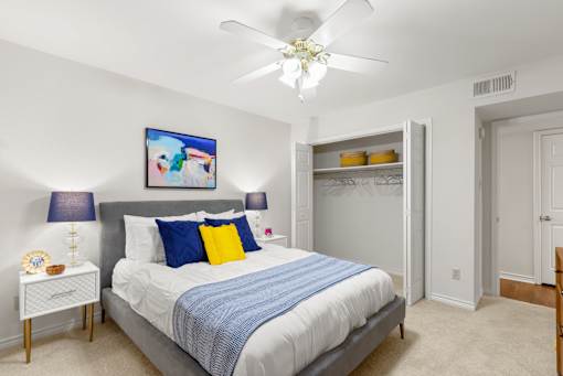 A bedroom with a bed, a ceiling fan, and a painting on the wall.