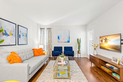 A living room with a grey couch, a blue chair, a glass coffee table and a painting on the wall.