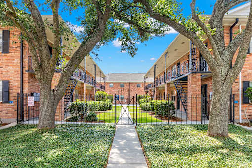 A courtyard with a pathway and trees in front of a brick building.