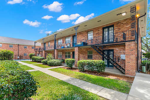 A sunny day at a brick apartment complex with green bushes and a clear blue sky.