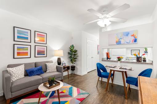 A living room with a grey couch, a coffee table, a dining table with chairs, a ceiling fan, and a painting on the wall.