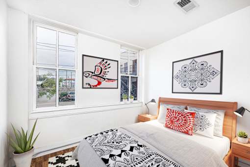 A bedroom with a bed, two pillows, a nightstand, and two framed pictures on the wall.