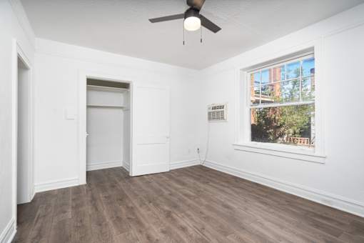 A room with a ceiling fan and a window showing trees outside.