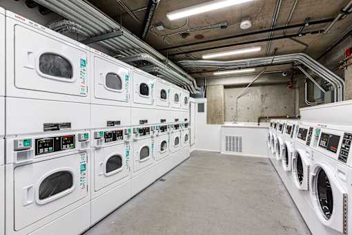 A row of white front loading washing machines are lined up in a laundromat.