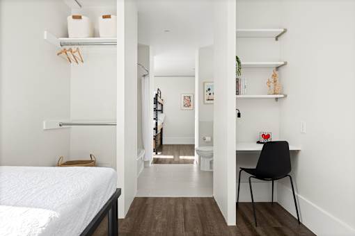 A white bedroom with a bed, desk, and shelves.