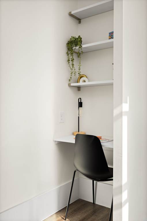 A black chair is in front of a white wall with a shelf above it.