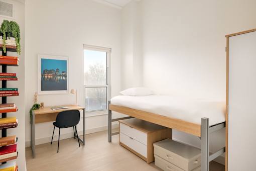 A bedroom with a bed, desk, chair, and a window.