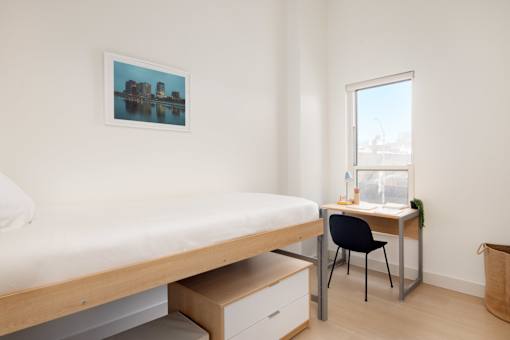 A bedroom with a bed, desk, chair, and a picture on the wall.