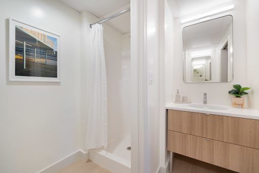 A bathroom with a white shower curtain and a wooden vanity with a mirror.