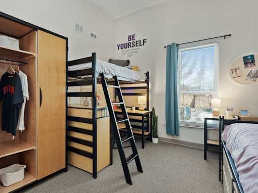 A room with bunk beds, a wardrobe, and a window with a view of a fence.