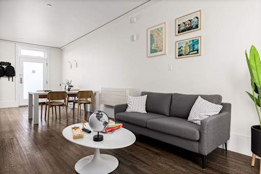 A living room with a grey couch, a white coffee table, and a dining table with chairs.