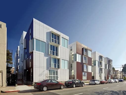 A row of modern apartment buildings with cars parked in front.