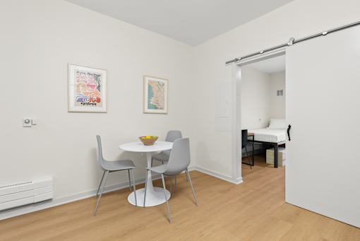 A white dining table with two chairs and a bowl of fruit on it.