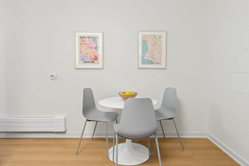 A dining table with four grey chairs and two pictures on the wall.