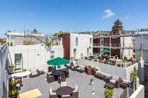 A rooftop patio with tables and chairs and a green umbrella.