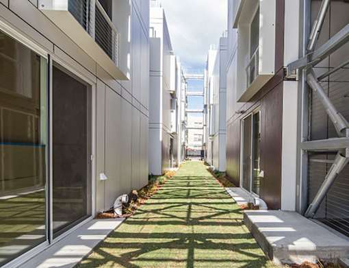 A long, narrow walkway between buildings with grass on either side.