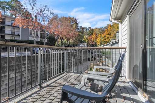 A balcony with a black chair and table is surrounded by a metal railing.