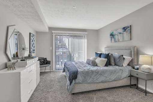 A bedroom with a large bed, a vanity with a mirror, and a window with blinds.