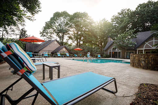a swimming pool with chairs and umbrellas in front of a house