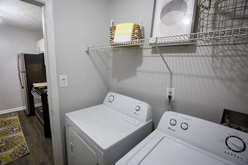 an empty laundry room with a washer and dryer and a shelf above it