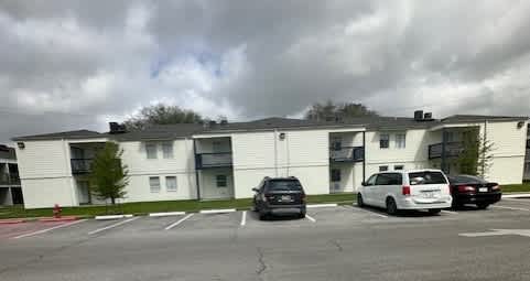 A parking lot in front of a white apartment building with cars parked.